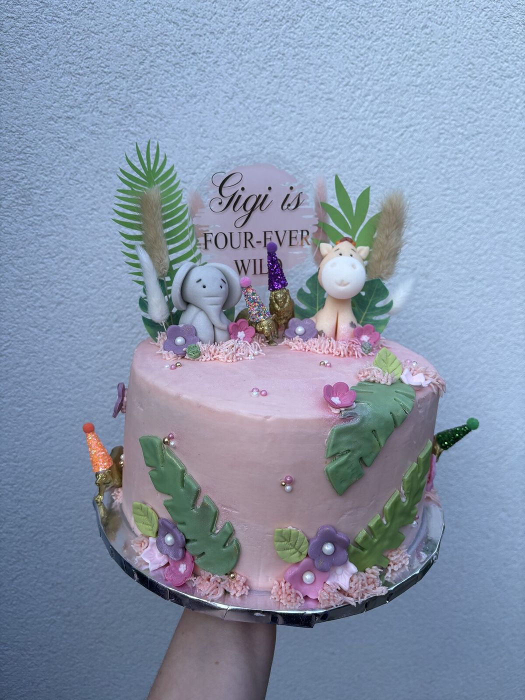 Pink jungle safari themed 4th birthday cake with fondant animals and tropical leaves