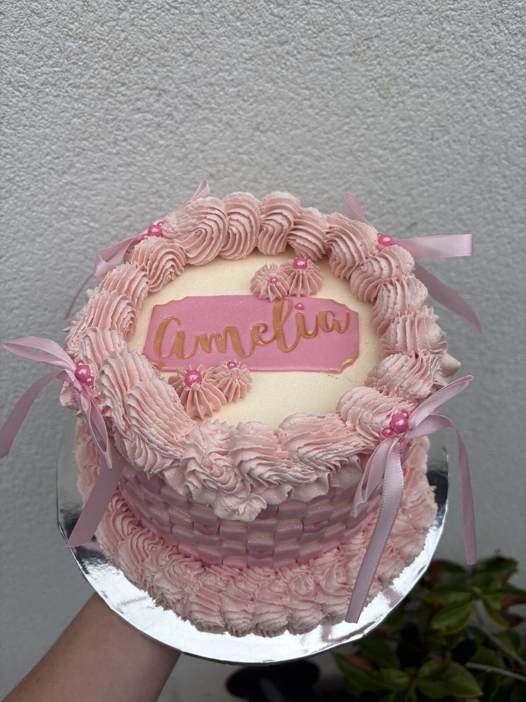 Pink buttercream cake with basket weave sides, ribbons and a personalised name plaque