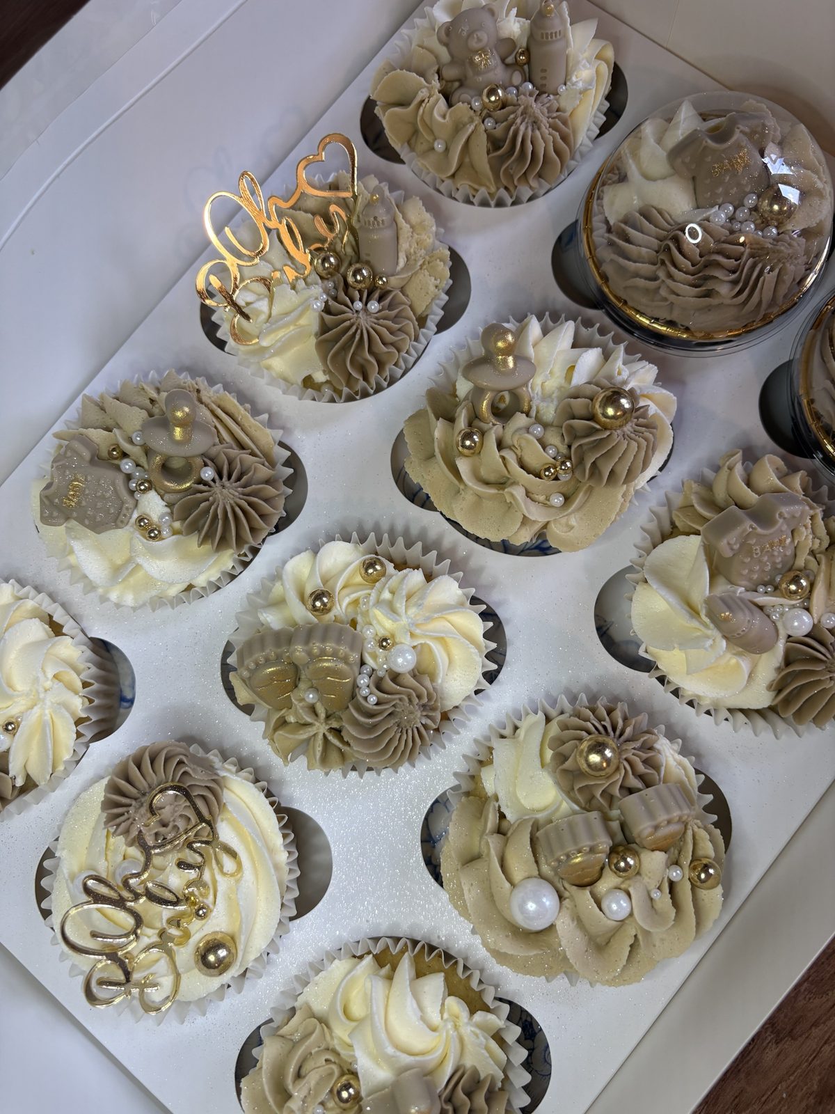 Gender reveal cupcakes in ivory and taupe buttercream with gold pearls, baby-themed toppers and Oh Baby gold toppers