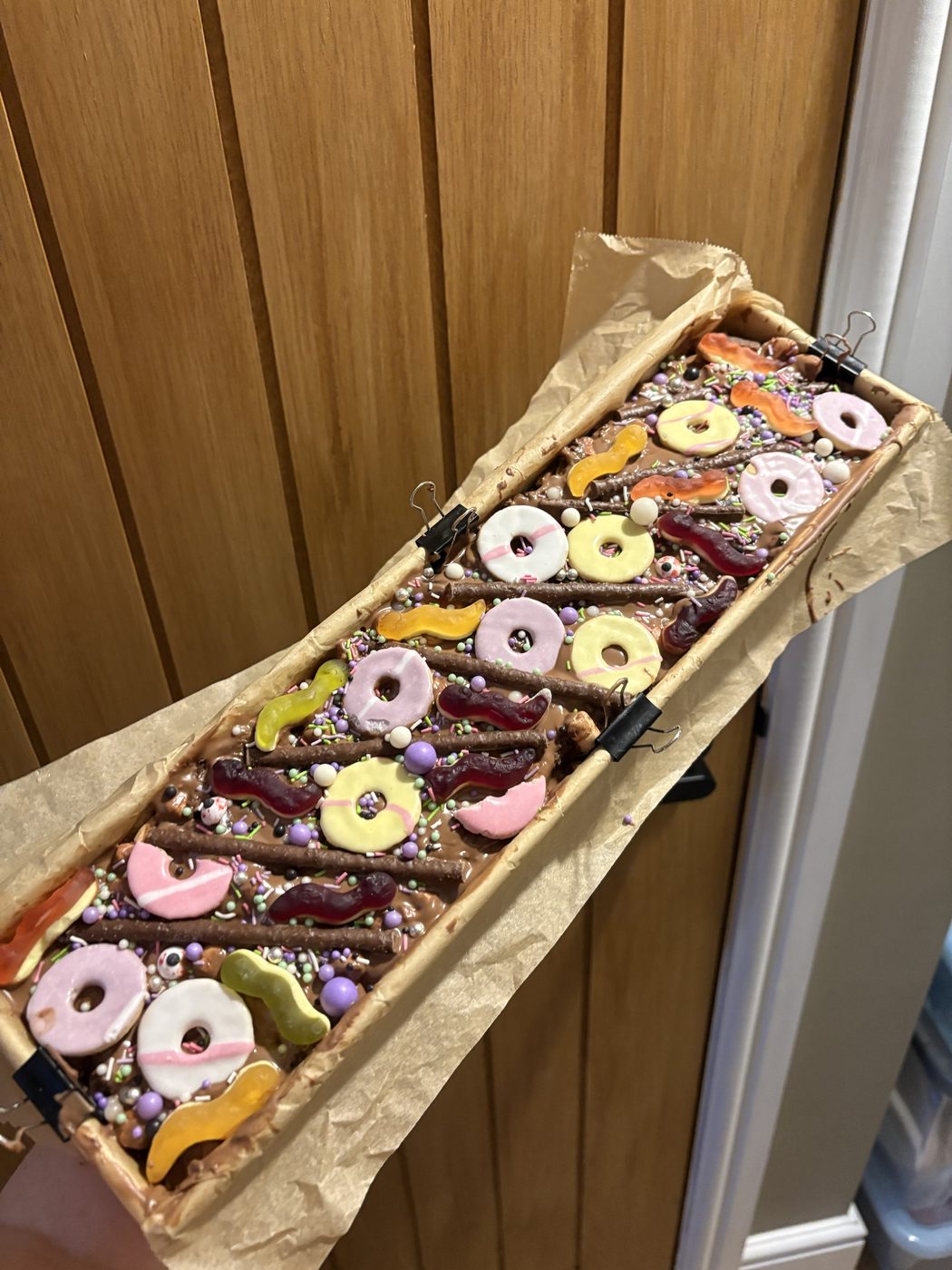 Milk chocolate rocky road tray bake topped with party ring biscuits, chocolate fingers, jelly sweets and sprinkles